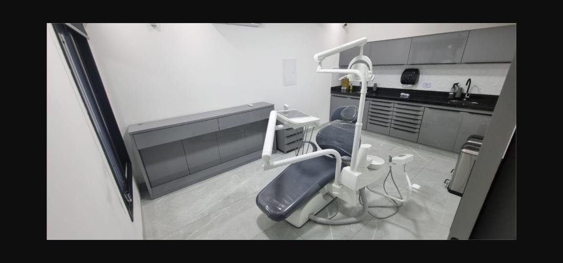Sala clínica com cadeira odontológica, bancada e armários cinza
