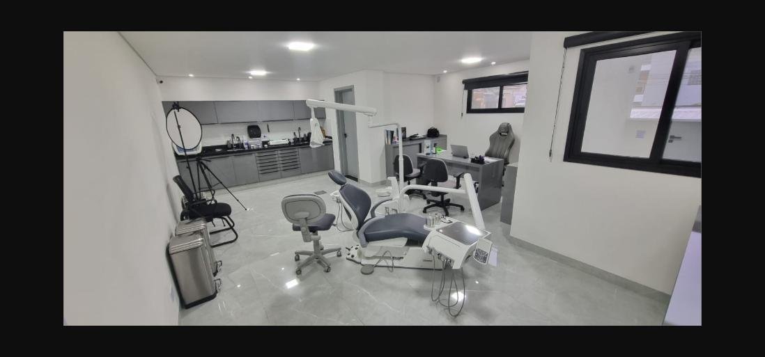 Sala clínica ampla com cadeira odontológica, mesa e equipamento de fotografia clínica